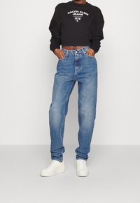 Black cropped sweatshirt with white logo; mid-rise, light blue denim jeans; loose fit; white sneakers with textured soles.