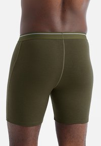 Olivgröna kalsonger gjorda av mjukt, stretchy tyg med en åtsittande design. Har en kontrasterande midja med en tunn rand.