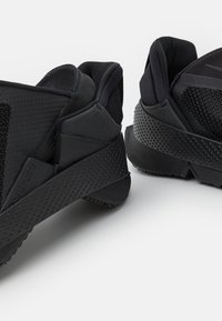 Juodi sportiniai bateliai su tekstūruota tinklelio viršumi, paminkštintu kraštu ir kontrastinga matinė ir blizgi guma su perforacijomis.