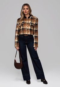 Kort jakke i struktureret brun og creme houndstooth mønster, med guldknapper; sat sammen med mørke brede jeans og en brun taske.