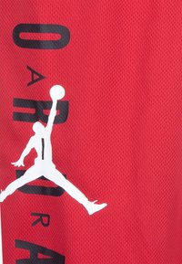 Rode mesh sporttrui met zwarte letters en een witte silhouet van een springende atleet die een basketbal vasthoudt.