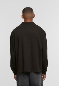 Black long-sleeve shirt with a collar, featuring a relaxed fit and a straight hemline. Soft texture and simple design without embellishments.