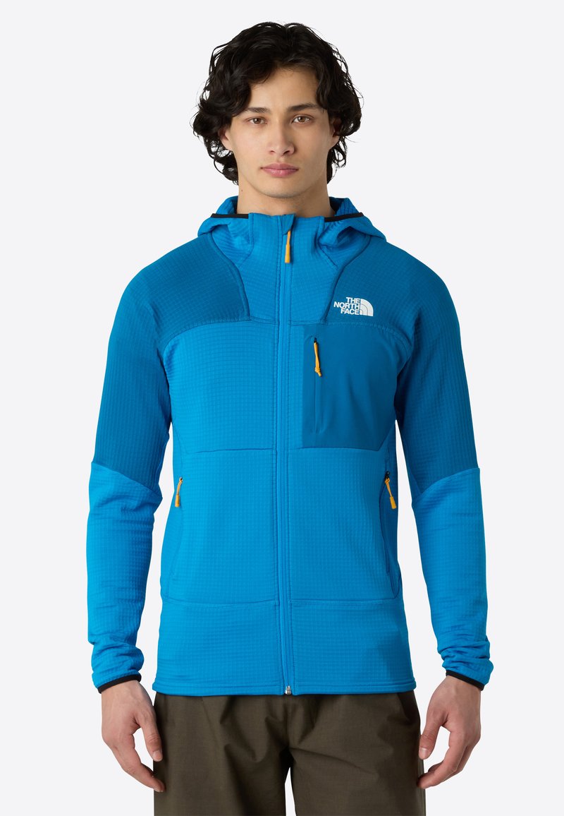 Giacca blu con zip caratterizzata da un design texturizzato, cappuccio e diverse tasche con cerniere gialle. Realizzata in un materiale leggero e traspirante.