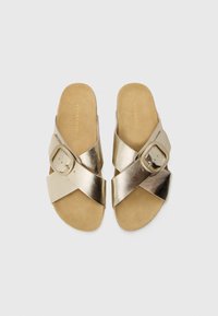 Gold cross-strap slide sandals with a flat sole. Features a large buckle accent and a soft, suede-like footbed for comfort.