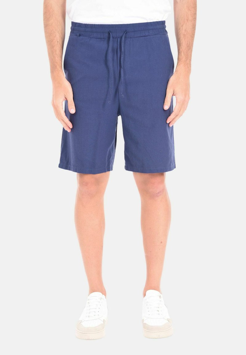 Pantaloni corti blu in lino con vita elastica e cordoncino. Presentano tasche laterali e una lunghezza sopra il ginocchio. Abbinati a sneakers bianche.
