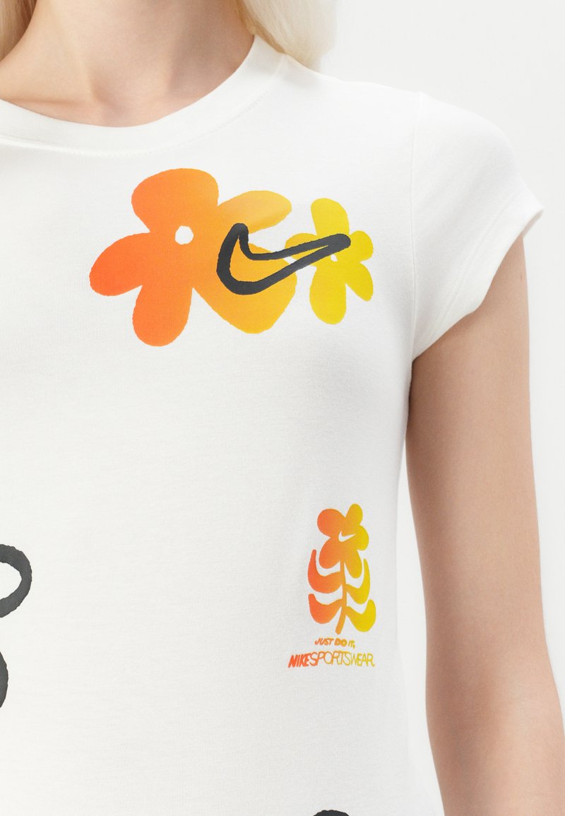 Biała bawełniana koszulka z krótkim rękawem, z wielokolorowymi grafikami kwiatowymi w odcieniach pomarańczowym i żółtym, z czarnym logo Nike oraz czerwonym detalem marki.