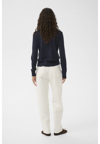 Marineblauer Rippenstrickpullover mit langen Ärmeln, kombiniert mit weißen, weit geschnittenen Hosen und dunkelbraunen Schuhen. Schlichtes Design, tailliert geschnitten.