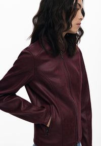 Burgundy faux leather jacket with a fitted design, high collar, zip closure, and side pockets, featuring subtle sheen and seam detailing.