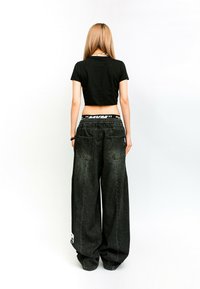 Camiseta negra corta de manga corta combinada con pantalones de chándal de denim gris oscuro de corte suelto, que cuentan con una cintura elástica y bolsillos traseros.