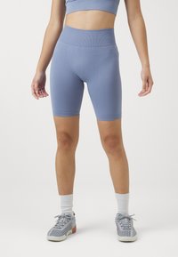 Kék kötött kerékpáros short, magas derékkal és sima textúrával, szürke sportcipővel és fehér bokazoknival párosítva.
