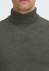 Dunkelgrüner Strickrollkragensweater mit gerippter Textur am Kragen und am Körper, mit glatter Oberfläche und figurbetontem Design.