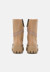 Botas de chuva gloss bege com uma faixa texturizada e fecho lateral. Sola robusta com ranhuras distintivas para aderência. Material suave e durável.
