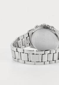 Montre en acier inoxydable argenté avec un bracelet poli. Boîtier rond avec couronne et poussoirs visibles ; dos lisse avec détails gravés.