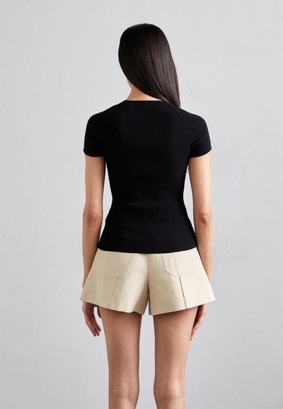 Zwarte ribgebreide top met korte mouwen, aansluitend model, gecombineerd met beige high-waisted shorts met achterzakken en geplooid detail aan de voorkant.