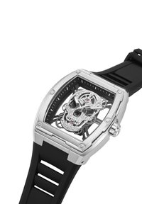 Skeletna ura s srebrnim kvadratnim ohišjem, črnim gumijastim paščkom in zapletenim motivom lobanje s kristalnimi poudarki ter vidnimi zobniki.