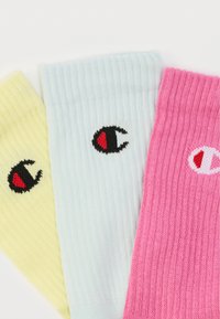 Τρεις ριγωτές κάλτσες σε κίτρινο, ανοιχτό μπλε και ροζ. Κάθε μία έχει ένα λογότυπο με μαύρο περίγραμμα και κόκκινες λεπτομέρειες. Μαλακή υφή υλικού.