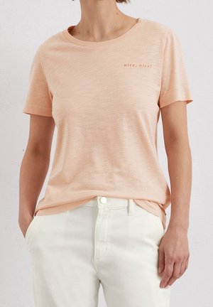 Brzoskwiniowy t-shirt z krótkim rękawem wykonany z lekkiego materiału, z okrągłym dekoltem i niewielkim nadrukiem "nice, nice!" na lewej piersi.