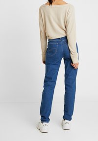 Pull en ribbed beige et jean droit bleu. Le jean a des poches arrière et une cheville légèrement fuselée. Des baskets blanches sont portées.