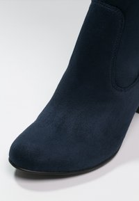 Navy blue suede ankle boot with a pointed toe, elastic side panel, and a slender, slightly curved heel. Smooth texture throughout.