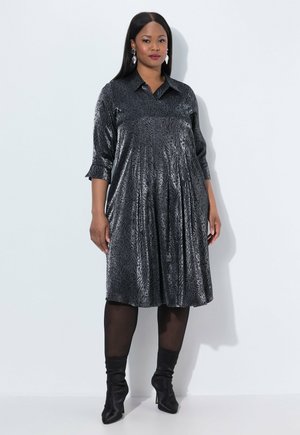 Schwarzes, gemustertes, knielanges Kleid mit Kragen, drei Viertelärmeln und Falten, kombiniert mit schwarzen Stiefeln mit Absatz und strukturiertem Stoff.