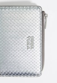 Metalen zilveren portemonnee met een quilted textuur, voorzien van een ritssluiting en een reliëf merknaam "BIMBA Y LOLA" aan de voorkant.