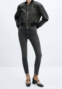 Cazadora bomber de cuero gris oscuro con puños acanalados, combinada con jeans ajustados gris oscuro y zapatos de charol negros de tacón cuadrado.