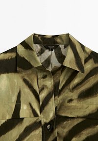 Olive green button-up shirt with a tiger stripe pattern in darker green. Features a classic collar and smooth, textured fabric.