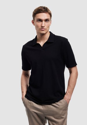 Sort kortærmet polo-shirt med struktureret stof, der har en åben krave og en afslappet pasform, parret med beige bukser.