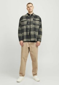 Schwarz-beige karierte Flanellhemden mit Knopfverschluss, zwei Brusttaschen und lockerer Passform, kombiniert mit beigen Hosen und weißen Sneakers.