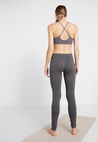 Brassiere sportivo grigio con un motivo a texture e schiena incrociata, abbinato a leggings grigi a vita alta, con una texture liscia e un design aderente.