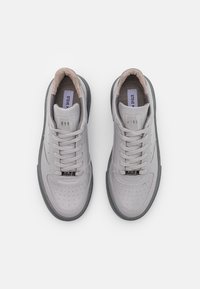 Helle graue Sneaker mit glattem Lederobermaterial, runder Zehenpartie, durchbrochenen Details und grauer Gummisohle. Die Schnürsenkel und das weiche Futter sind in kontrastierendem Beige.