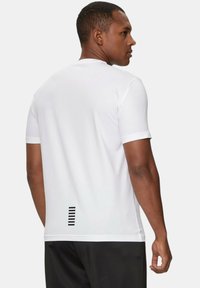 T-shirt bianco a maniche corte realizzato in tessuto leggero. Presenta un dettaglio a righe orizzontali nere sul retro, vicino all'orlo.