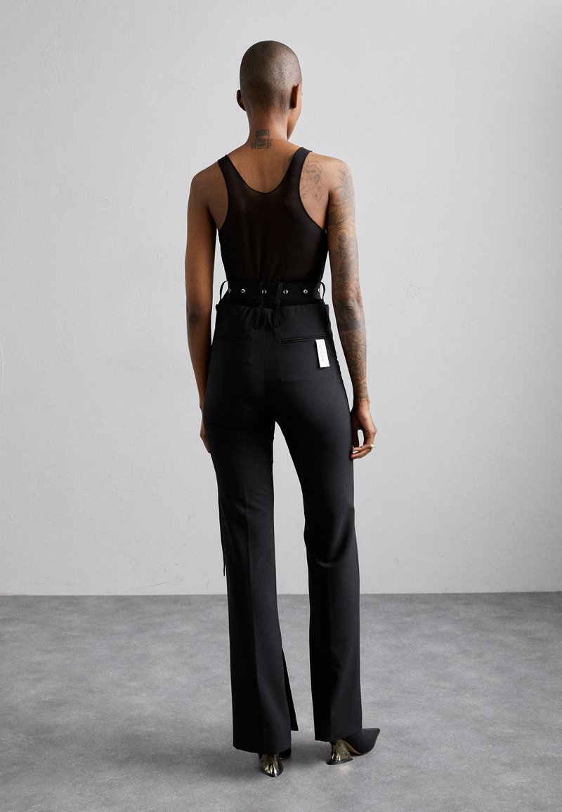 Débardeur en mesh noir avec une taille ajustée et des détails de ceinture, associé à un pantalon noir taille haute avec des jambes évasées et des accents de fermeture éclair.