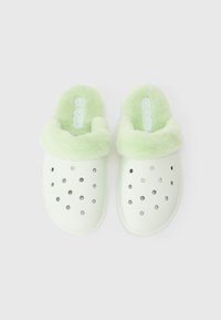Ett par ljusgröna Crocs-tofflor med plyschfoder och ventilationshål, visade ovanifrån på en vit bakgrund.