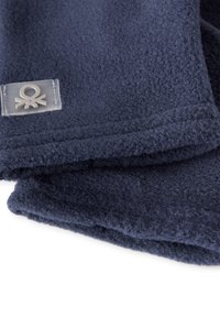 Granatowy szalik polarowy o gładkiej fakturze i zaokrąglonych krawędziach, z małą, przezroczystą metką z minimalistycznym logo.