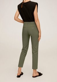 Groene slim-fit broek met achterzakken en decoratieve knopen, in combinatie met een zwart topje met korte mouwen. Glad materiaal en op maat gemaakt ontwerp.