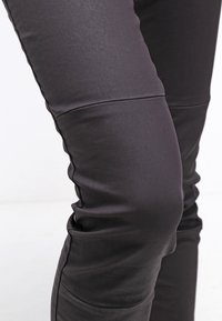 Svarta tights med en slät textur, med sydda knäakcent och en figurnära design. Närbild visar tygens glans.