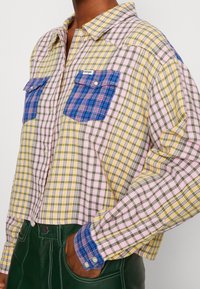 Karierter Hemd mit gelben, grünen, pinken und blauen Mustern. Eine blaue Karottentasche, Knopfverschluss, Kragen-Design und lange Ärmel.