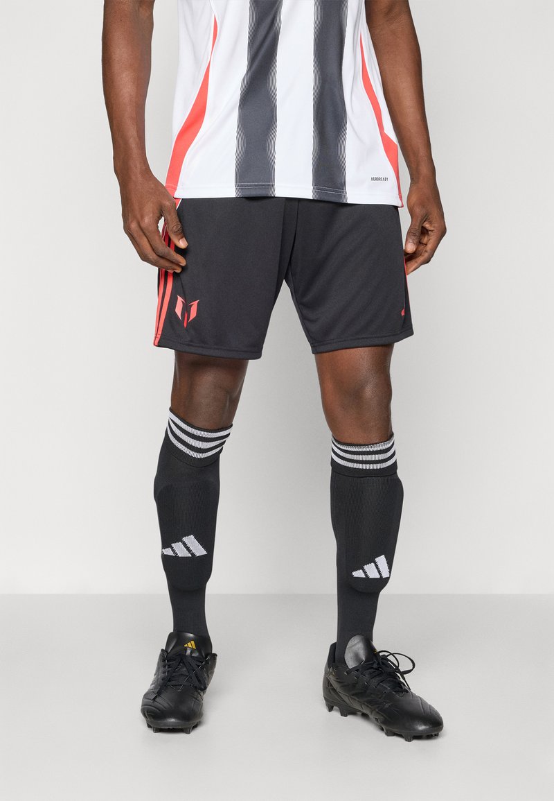 Schwarze Fußballshorts mit roten Akzenten, kombiniert mit schwarzen knielangen Socken mit weißen Streifen und schwarzen Fußballschuhen mit gelben Details.