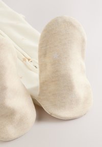 Kreemivärvi pehmeast kangast saabastega, mille talladel on tähe mustrid, ümardatud otsade ja õmblusteta disainiga.