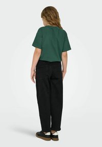 Zelené bavlněné tričko s krátkým rukávem je kombinováno s černými džínami s vysokým pasem. Oblečení doplňují černé tenisky s bílými detaily.