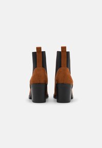 Bottines en suede marron avec un panneau élastique noir, bout carré et un large talon noir, dotées d'une languette à l'arrière pour un enfilage facile.