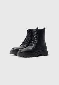 Bottes de cheville en cuir noir avec bout rond, surface texturée, devant à lacets et semelle en caoutchouc robuste dotée d'un design à crampons imposants.