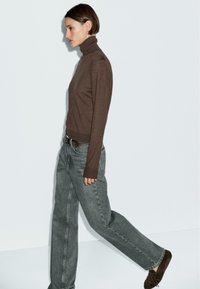 Maglione marrone a collo alto abbinato a jeans in denim grigio chiaro a vita alta e mocassini in suede marroni. Design semplice, texture liscia.