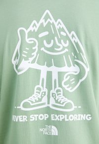 Lys grøn t-shirt med en hvid tegneserie bjergkarakter, der giver tommelfinger op, teksten "STOP ALDRIG MED AT UDFORSKE" og et brandlogo.