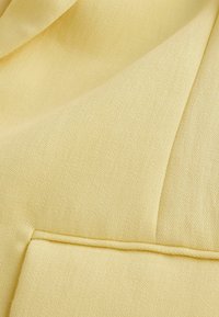 Tela suave de color amarillo pálido con una superficie texturizada, mostrando una costura doblada y una superposición estructurada.