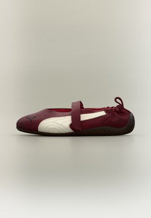 Jeden bordovo-biely slip-on topánok s elastickým zadným dielom, remienkom cez vrch a textúrovanou čiernou podrážkou na neutrálnej farbe pozadia.