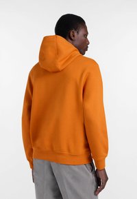 Pomarańczowa bluza z kapturem na sznurku, z prążkowanymi mankietami i dołem, wykonana z miękkiego materiału, o luźnym kroju i minimalistycznym wzornictwie.