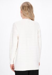 Cardigan crema a maniche lunghe realizzato in materiale a maglia testurizzato con strisce orizzontali, dotato di scollatura rotonda e spacchi laterali.