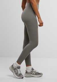 Leggings taille haute et ajustés en tissu gris sobre avec une texture lisse. Associés à des sneakers de sport gris et blanc.